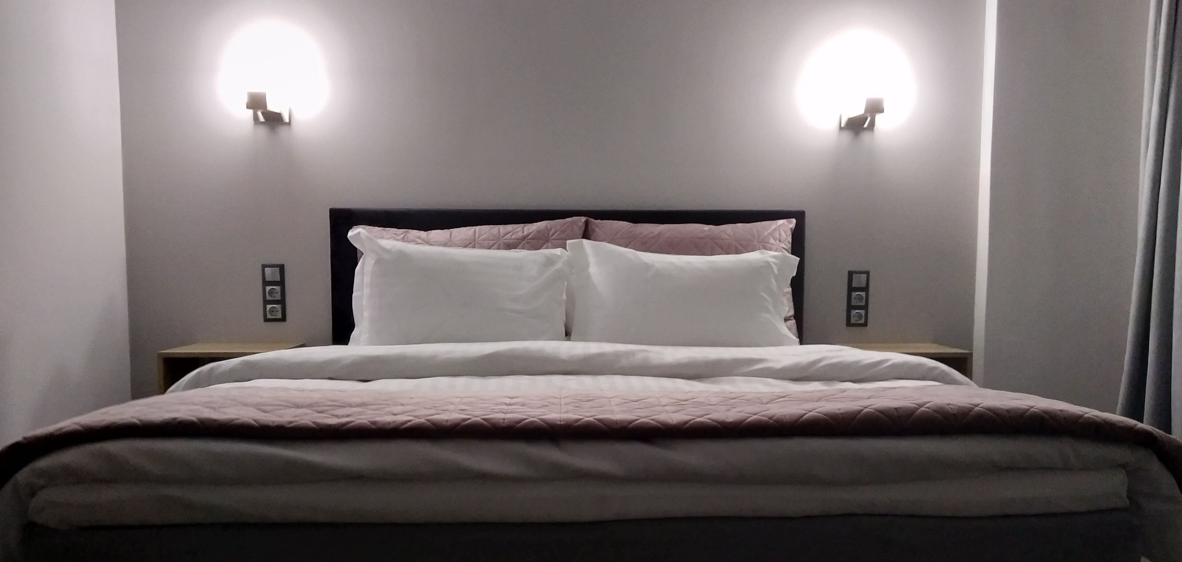 Ein ordentlich bezogenes Bett mit Kopfteil, zwei Nachttischen und Wandleuchten.