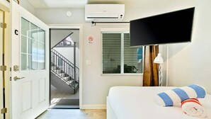 Ein Hotelzimmer mit Bett, Fernseher, Klimaanlage, Treppe und Fenster mit Jalousien.