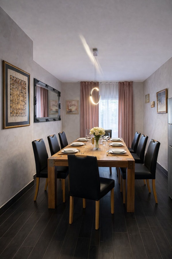 Un comedor con mesa de madera, sillas negras, un jarrón de flores y cuadros en las paredes.
