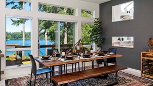 A dining area with a wooden table set for four, large windows with a view of a lake and trees, and a dark gray accent wall with a kitchen backsplash visible. - New Listing! Amazing Lakefront 4 Bedroom 4 1/2 Bath,Sleeps 10, w/ Bonus room,Incredible Views,Dock (Florence)