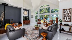A modern living room with a fireplace, large windows, and a mix of leather and wooden furniture. - New Listing! Amazing Lakefront 4 Bedroom 4 1/2 Bath,Sleeps 10, w/ Bonus room,Incredible Views,Dock (Florence)