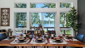 A dining room with a large table set for a meal, large windows with a view of trees and water, and a decorative wall piece. - New Listing! Amazing Lakefront 4 Bedroom 4 1/2 Bath,Sleeps 10, w/ Bonus room,Incredible Views,Dock (Florence)