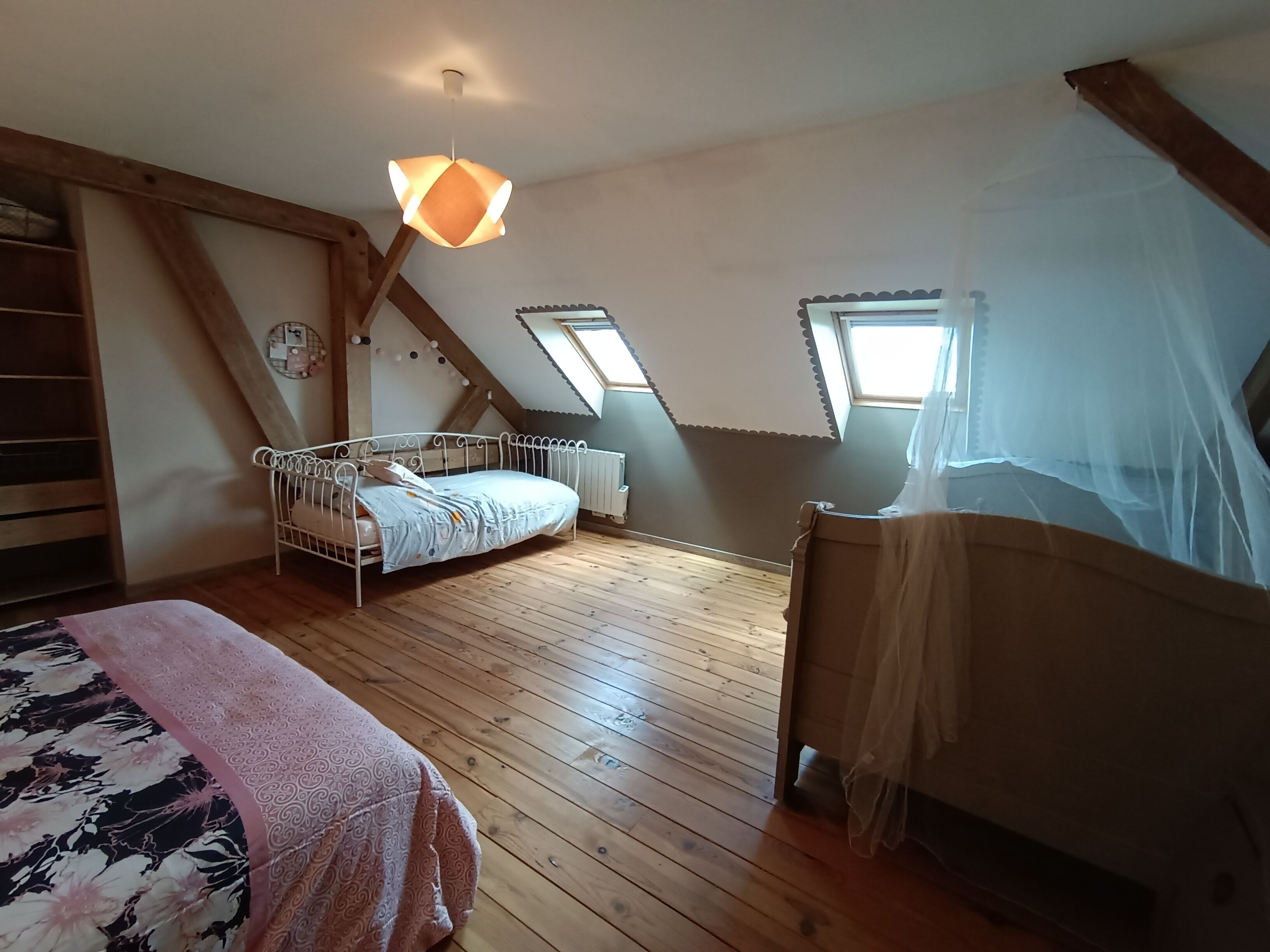 A bedroom with a sloped ceiling, a bed, a window, and a wooden floor.