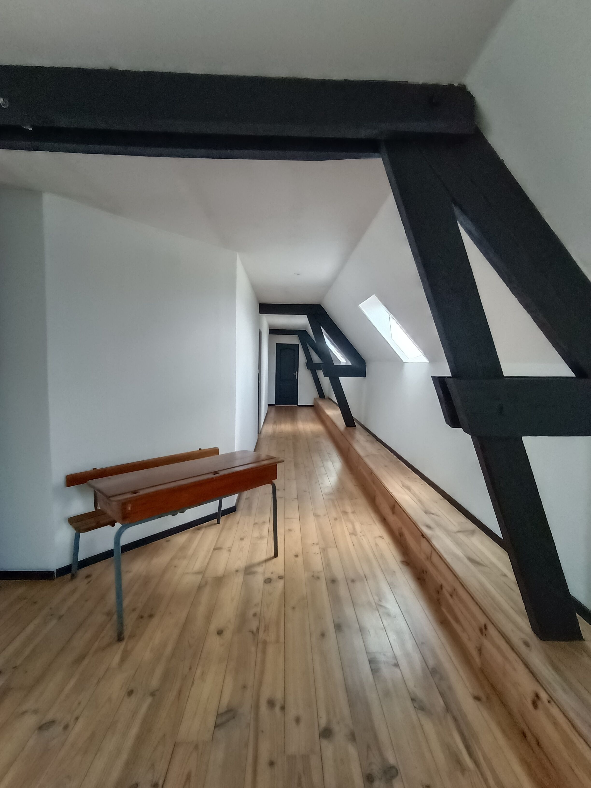 An attic room with wooden flooring, a slanted ceiling, and a bench.