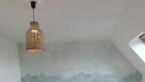 Ein Schlafzimmer mit einem Bett, zwei Nachttischlampen, einer Pendelleuchte und einem Wandgemälde.
