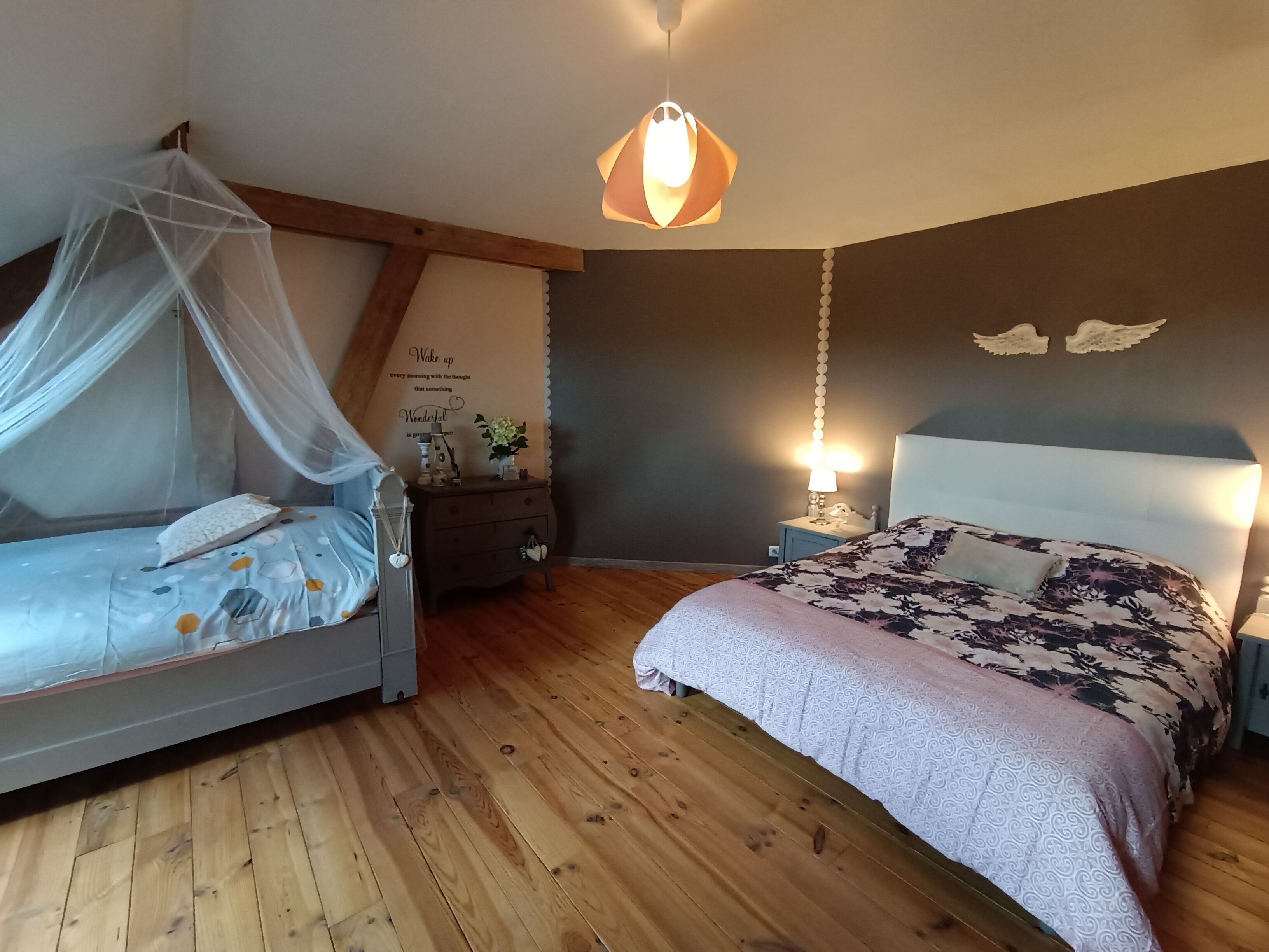 A bedroom with a canopy bed, a bedside table with a lamp, and a wall with decorative elements.
