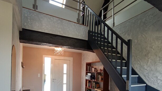 Ein geräumiger Wohnbereich mit Treppe, einer Chandelieber und einem Bücherregal.