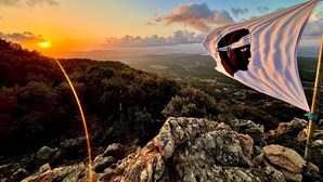 Eine Berglandschaft im Abendrot, mit felsigem Gelände und einer Fahne mit Silhouette.