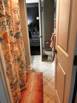 Ein Badezimmer mit Toilette, einem Handtuchhalter mit Handtüchern, einem Duschvorhang mit nautischen Motiven und einem Teppich auf dem Boden.