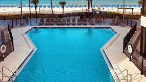 Una piscina con vista a la playa, sillas de descanso y palmeras.
