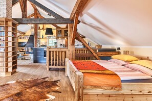 A loft bedroom with exposed wooden beams, a lofted kitchen, and a large window. - Ferienwohnung mit Balkon und Bergblick (Bad Feilnbach)