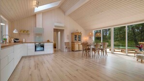 A spacious kitchen with wooden flooring, a dining area with wicker chairs, and large windows offering a view of the outdoors. - Traumhaus Römö für 6 Personen. Unesco Wattenmeer (Rømø)