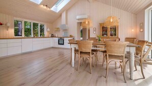 A spacious kitchen with white cabinets, a dining area with wicker chairs, and a skylight. - Traumhaus Römö für 6 Personen. Unesco Wattenmeer (Rømø)