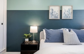 A bedroom with a bed, a bedside table with a lamp, and two framed pictures on the wall.
