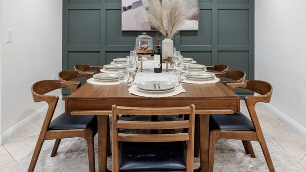 A dining room with a rectangular table set for six, surrounded by wooden chairs with cushioned seats.
