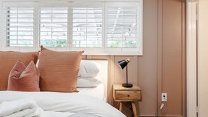 A bedroom with a bed, pillows, a nightstand with a lamp, and a window with blinds.
