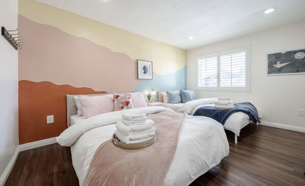 Un dormitorio con dos camas, un mural en la pared y una ventana con persianas.