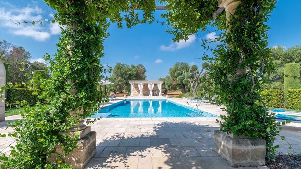 Una piscina con estructura de pérgola, rodeada de senderos de piedra y vegetación.