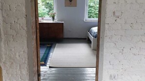 Une pièce dotée d’une porte en bois qui donne sur un espace comprenant une fenêtre, un lit et un luminaire fixé au mur.