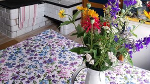 Une cuisine avec un mur recouvert de briques blanches, une porte en bois et une nappe à motifs floraux.