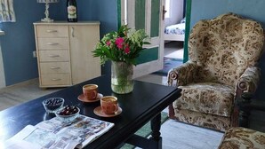 Une pièce avec un mur bleu, un meuble en bois, un fauteuil à motifs, une table avec un journal et un vase rempli de fleurs.