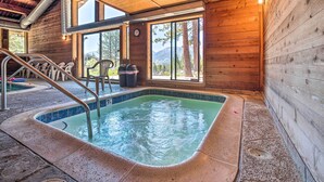 Une cabane en bois dotée d’un bain à remous, de murs en bois et de grandes fenêtres donnant sur une région montagneuse.