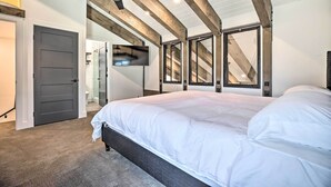 Une chambre avec un grand lit, des poutres apparentes, un ventilateur de plafond et un téléviseur fixé au mur.