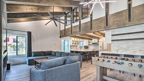 Un salon moderne avec un canapé d’angle, une table de baby-foot et une cuisine en arrière-plan.
