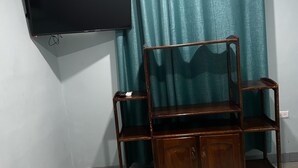 A room with a bed, a wooden cabinet, a TV mounted on the wall, and a curtain.