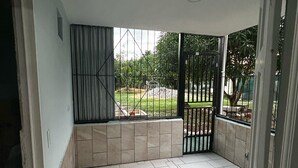A covered outdoor area with tiled flooring, a metal gate, and a view of greenery.