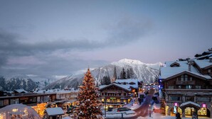 Un pueblo cubierto de nieve con un árbol de Navidad destacado, una montaña al fondo y edificios con letreros.