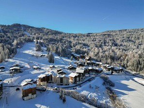 A snow-covered ski resort with multiple lodges, ski lifts, and a clear view of the surrounding forested mountains.