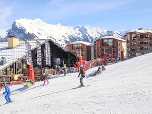 Une station de ski avec des pistes enneigées, un restaurant doté d’une terrasse et des bâtiments avec des balcons.