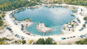 An aerial view of a circular lake surrounded by a parking area and a small island with a dock. - Quaint little home (La Grange)
