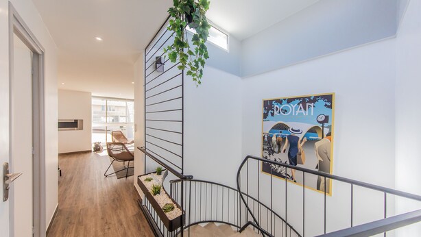 A staircase with a metal railing, a hanging plant, and a poster on the wall. - Le Foncillon 4* Apartment at the foot of the beach (Royan)