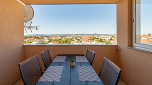 Ein Balkon mit Tisch und Stühlen, mit Blick auf ein Wohngebiet mit Häusern und blauem Himmel.
