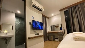 Una habitación de hotel con cama, escritorio, televisión, espejo y aire acondicionado.