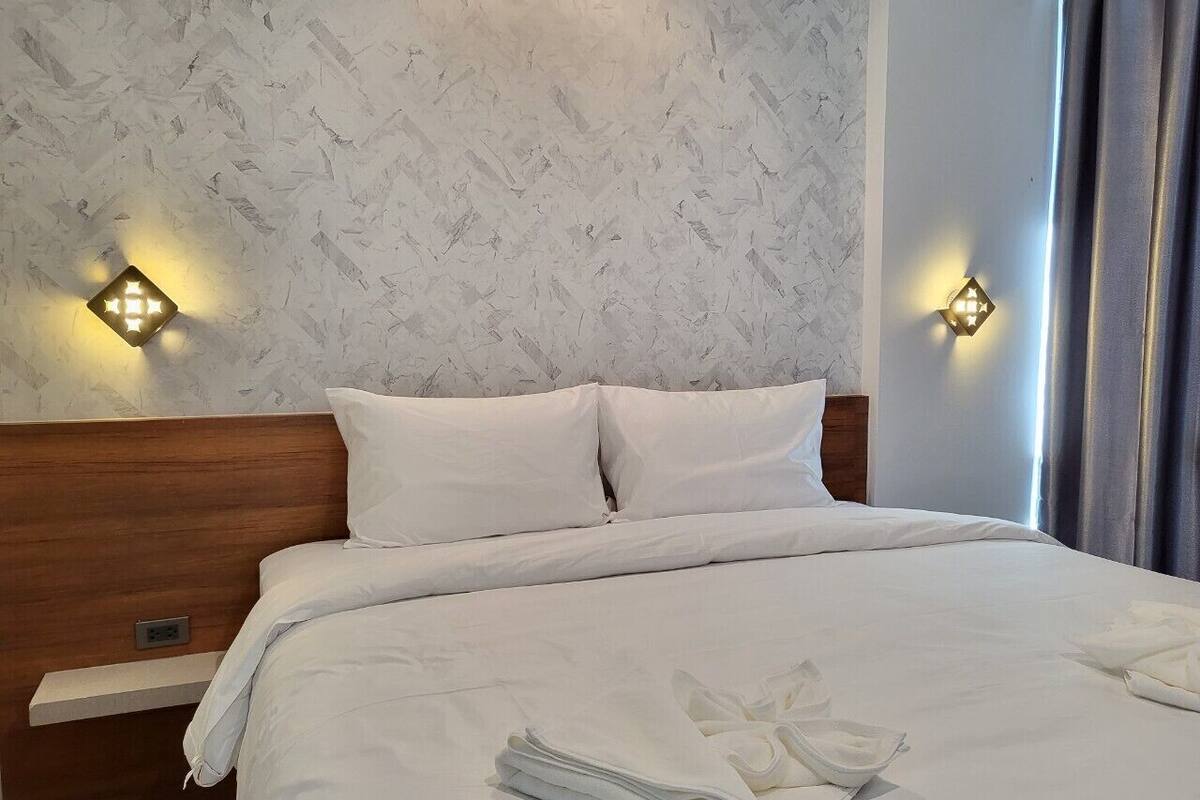 A neatly made bed with white linens, two wall-mounted light fixtures, and a wooden headboard.