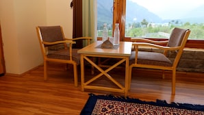 A wooden table with two chairs, a patterned rug, and a view of mountains through a window. - Zaara resort, hidden resort in manali (Manali)
