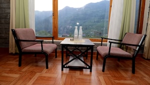 A room with two striped chairs, a table with a candle holder, and a view of mountains through a large window. - Zaara resort, hidden resort in manali (Manali)