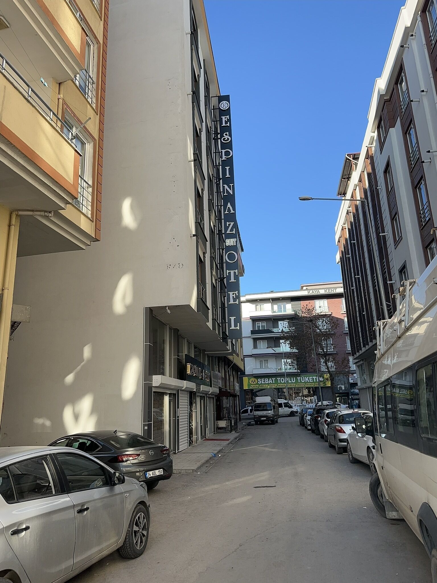 Une vue de rue avec un bâtiment portant l’inscription « Pinarotel » et un magasin appelé « Sebat Toplu Tuketim ».