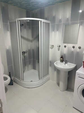 A bathroom with a glass-enclosed shower, a sink, a mirror, and a washing machine. - Espinaz Apart Otel  (Van)