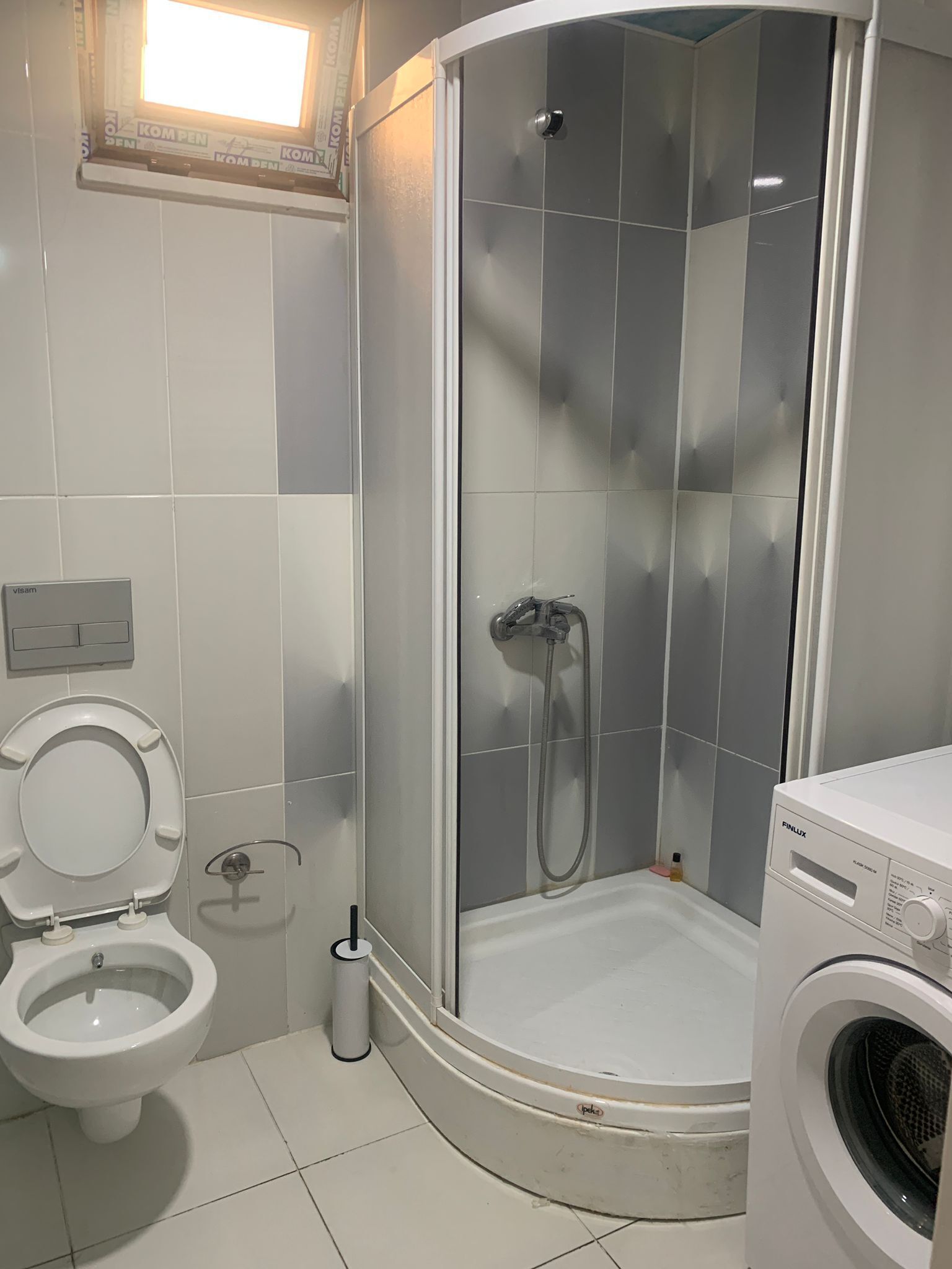 A modern bathroom with a toilet, a shower with a glass door, and a washing machine.