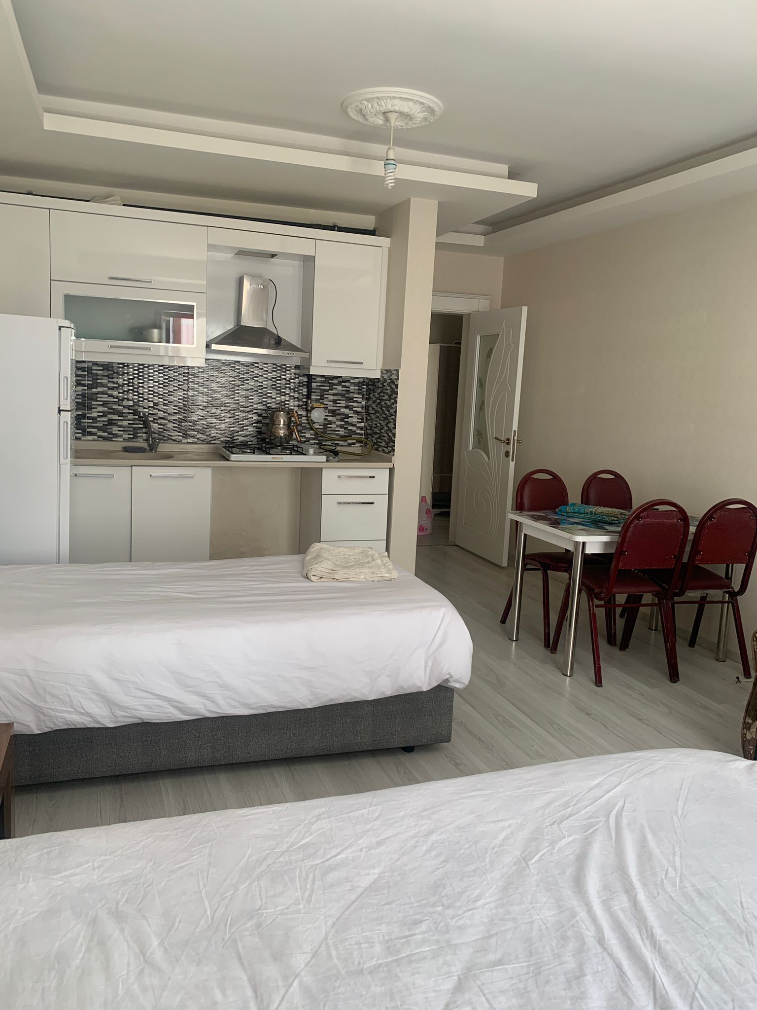 Habitación de hotel moderna con cama, una kitchenette pequeña, una mesa de comedor con sillas y un baño visible a través de una puerta abierta.