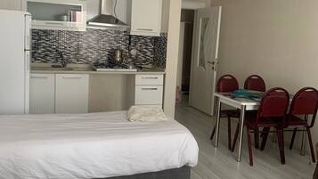 Habitación de hotel moderna con cama, una kitchenette pequeña, una mesa de comedor con sillas y un baño visible a través de una puerta abierta.