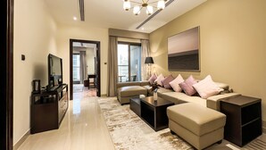 Una sala de estar moderna con un sofá, una mesa de centro y un televisor. Se aprecia un ventanal con cortinas, un candelabro y un cuadro en la pared.