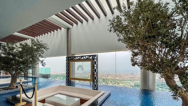 An infinity pool with a view of the city, a seating area, and a framed picture on the wall. - Luton Vacation Homes - Paramount Midtown (Dubai)