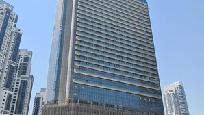 A tall, modern skyscraper with a glass facade and a prominent logo at the top. - Luton Vacation Homes - Paramount Midtown (Dubai)