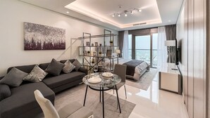 A modern living room with a sofa, coffee table, and a dining area. There is a large window with a view of the city. - Luton Vacation Homes - Paramount Midtown (Dubai)