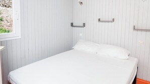 En säng för en person med vita sängkläder i ett rum med vertikala paneler på väggarna.